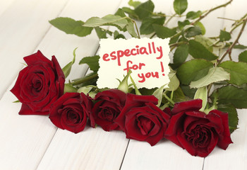 bouquet of red roses with note on a white wooden table close-up
