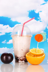 Delicious milk shake with fruit on table on sky background