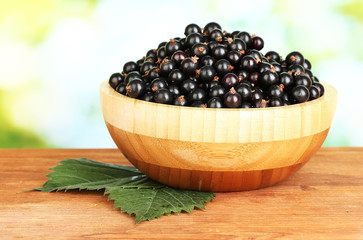 Fresh black currant in wooden bowl on green background close-up