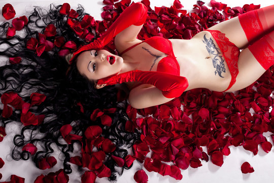 girl with tattoos in red lingerie in the petals of red roses