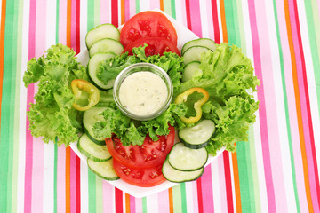 Chopped vegetables and sauce on plate on striped tablecloth