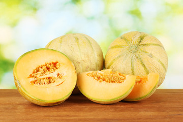 Cut melon on wooden table on green background