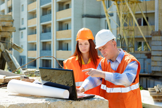Female architect and construction worker looking at laptop toget