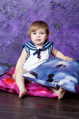 Fototapeta premium little girl in a dress in sea style sits on color pillows