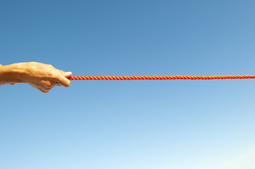 Hand pulling on rope sky background