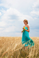 Naklejka premium Pretty girl with sunflower walking through the wheat field