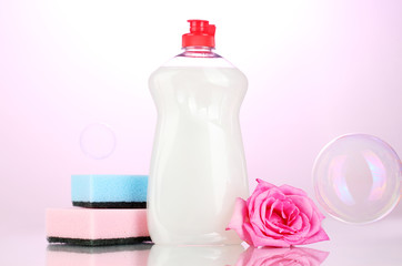 Obraz na płótnie Canvas Dishwashing liquid with sponges and flower on pink background