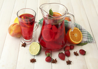 sangria in jar and glass with fruits, on white wooden table