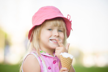 Adorable girl in pink hat eat ice cream sitting on grass