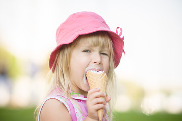 Adorable girl in pink hat eat ice cream sitting on grass