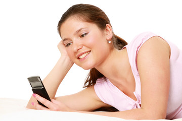 Excited young woman reading message lying on bed isolated