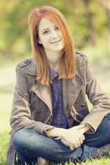 Obraz premium Beautiful red-haired girl sitting at green grass at park.