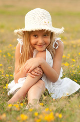 Cute little girl sitting on the meadow on sunny day