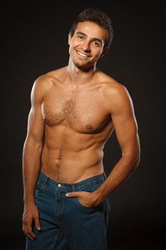 Young smiling muscular male shirtless with hand in pocket