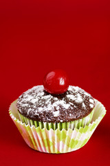 One chocolate cupcake with cherry over red