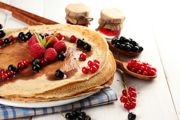 Delicious pancakes with berries and jam on plate on wooden