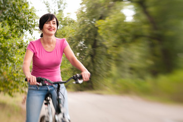 Woman riding bike on the summer forest road. Lensbaby effect