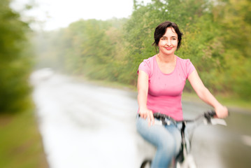 Woman riding bike on the rainy forest road. Lensbaby effect