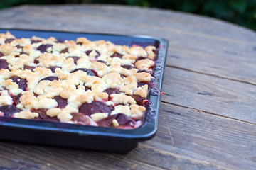 Fresh baked plum cake on oven tray and wooden table