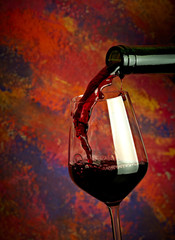 Fototapeta na wymiar Red wine pouring in glass over grange background