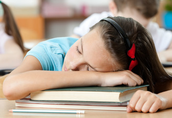 Tired schoolgirl sleeps at the desk, close up