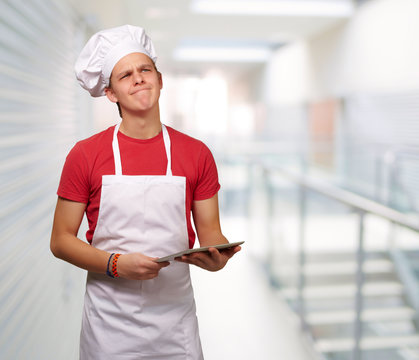 portrait of young cook man holding a digital tablet and thinking