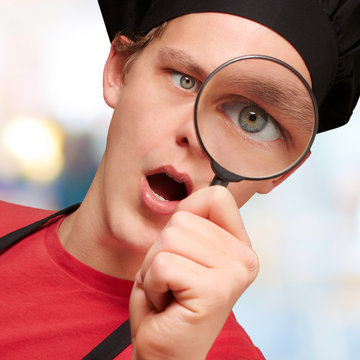 portrait of young cook man looking through a magnifying glass in
