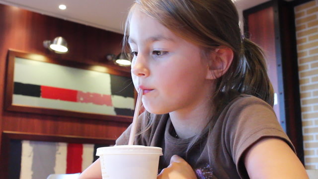 Nice young girl  drinks from plastic cup through straw