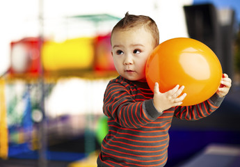 portrait of funny kid holding a big orange balloon against a abs