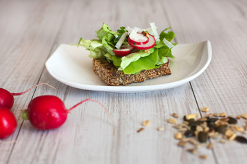Healthy sandwich with salad, radish and pumpkin seeds on wooden