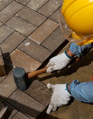 road worker in yellow helmet lays tile pavement