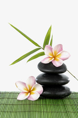 Zen stones and frangipani with bamboo leaf on green mat