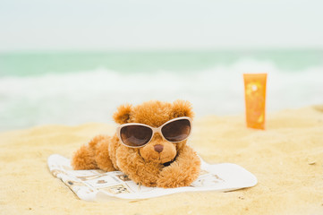 Teddy bear is sunbathing at the beach with sun screen on background