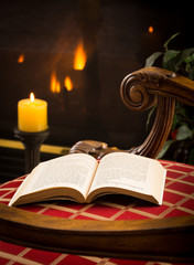 Paperback book open on chair by fire and candle