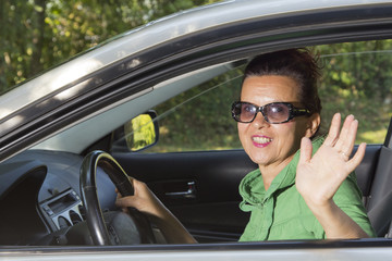 Friendly  woman looking out of car and waving hand