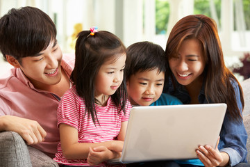 Obraz premium Chinese Family Using Laptop Whilst Relaxing On Sofa At Home
