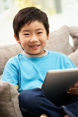 Young Chinese Boy Using Tablet Computer Whilst Sitting On Sofa