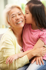 Chinese Grandmother And Granddaughter Relaxing On Sofa At Home