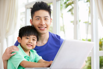 Chinese Father And Son Sitting At Desk Using Laptop At Home