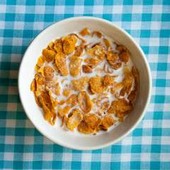 Breakfast bowl of cornflakes with milk on blue table cloth