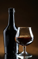 Glass of brandy and bottle on brown background