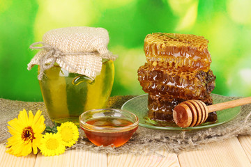 Jar of honey and honeycomb on wooden table on nature background