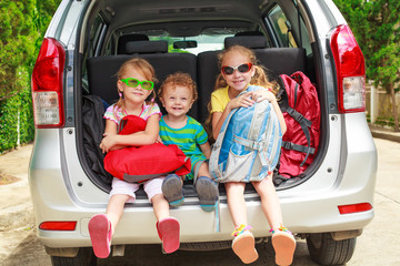 two little girls  and boy sitting in the car with backpacks