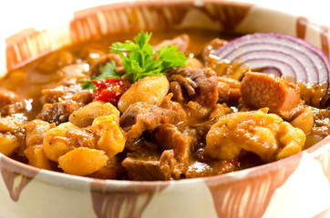 Goulash in clay pot against white background