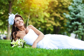 happy bride in white dress lying on green grass