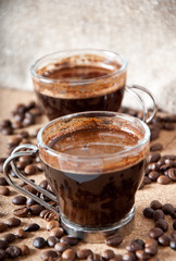 Two cups of black coffee on brown background 