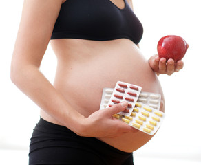 Ernährung in der Schwangerschaft - Nahrungsergänzung - schwangere Frau hält Tabletten und Apfel...