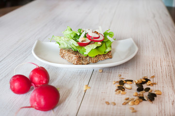 Fototapeta na wymiar Healthy sandwich with salad, radish and pumpkin seeds on wooden