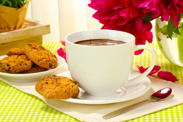 cup hot chocolate, cookies  and flowers on table in cafe