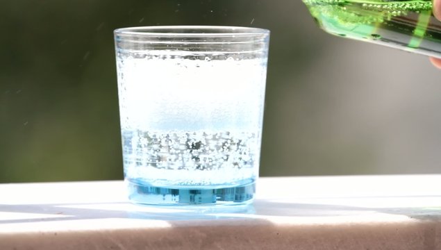 Mineral water pouring from bottle in glass with bubbles